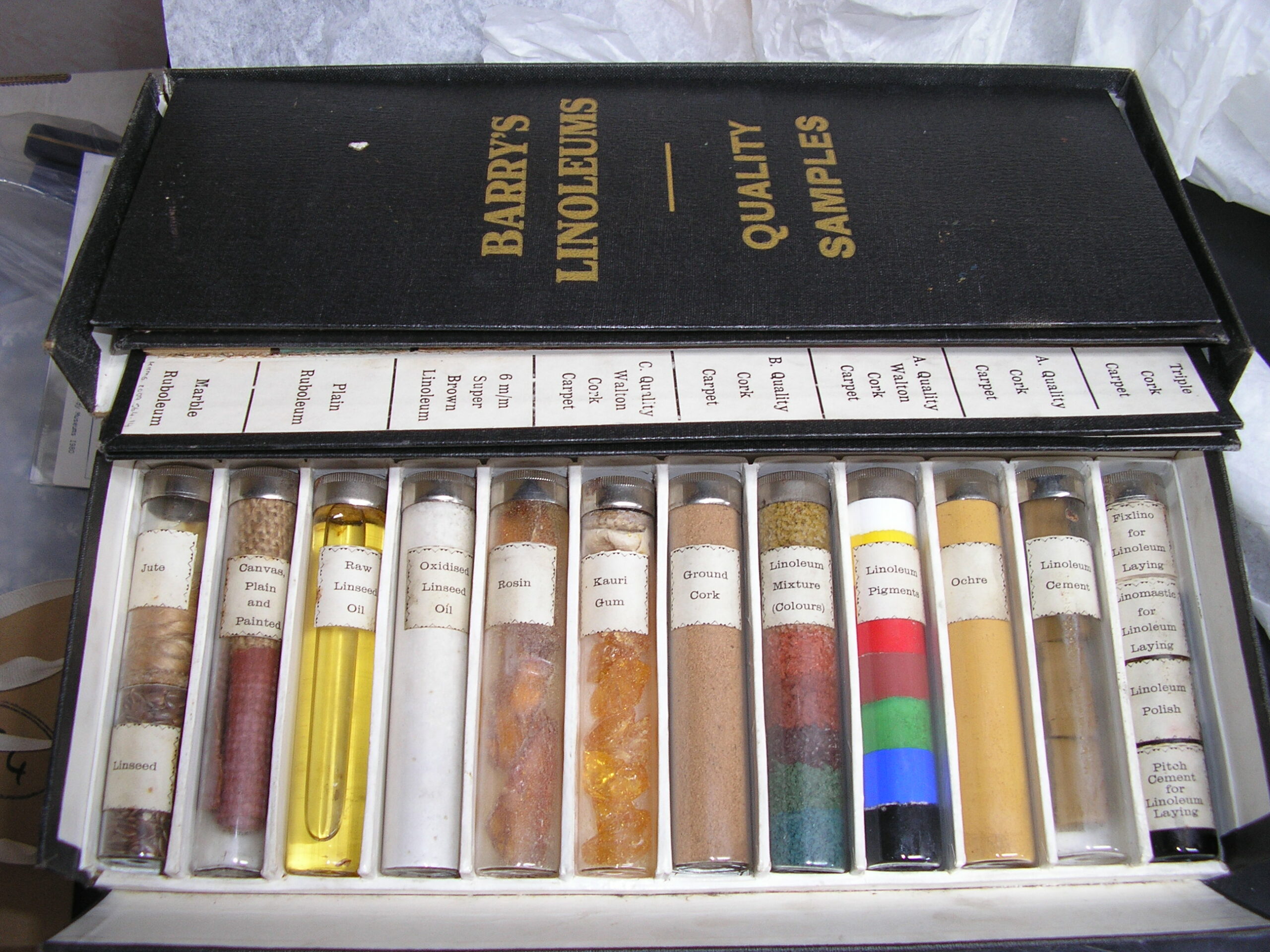 A black case containing several glass vials. Each vial is filled with a different colour substance, and is marked with a white label which describes the contents.